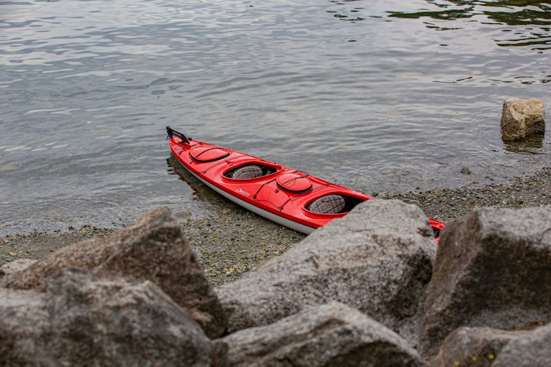 a red kayak sitting on the shore of a lake