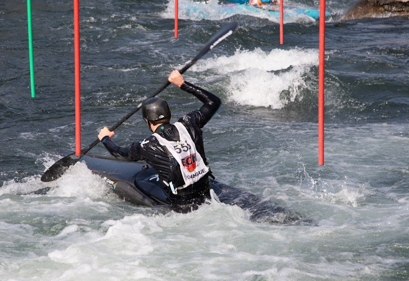 Person kayaking through whitewater rapids with gates.
