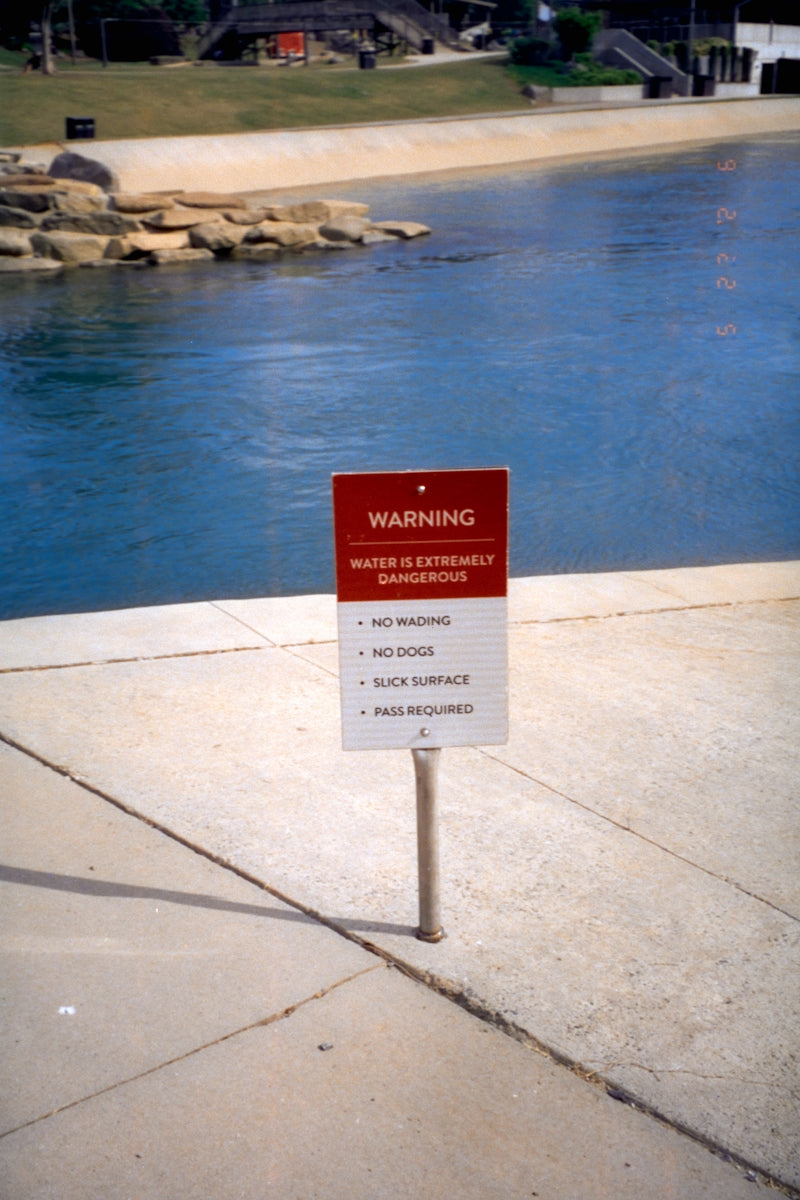 A red warning sign stands beside dangerous water.